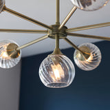 Endon Georgiana 8 light pendant shown close-up with brass spoke arms and spiral-cut clear glass globe shades against a navy and grey wall.