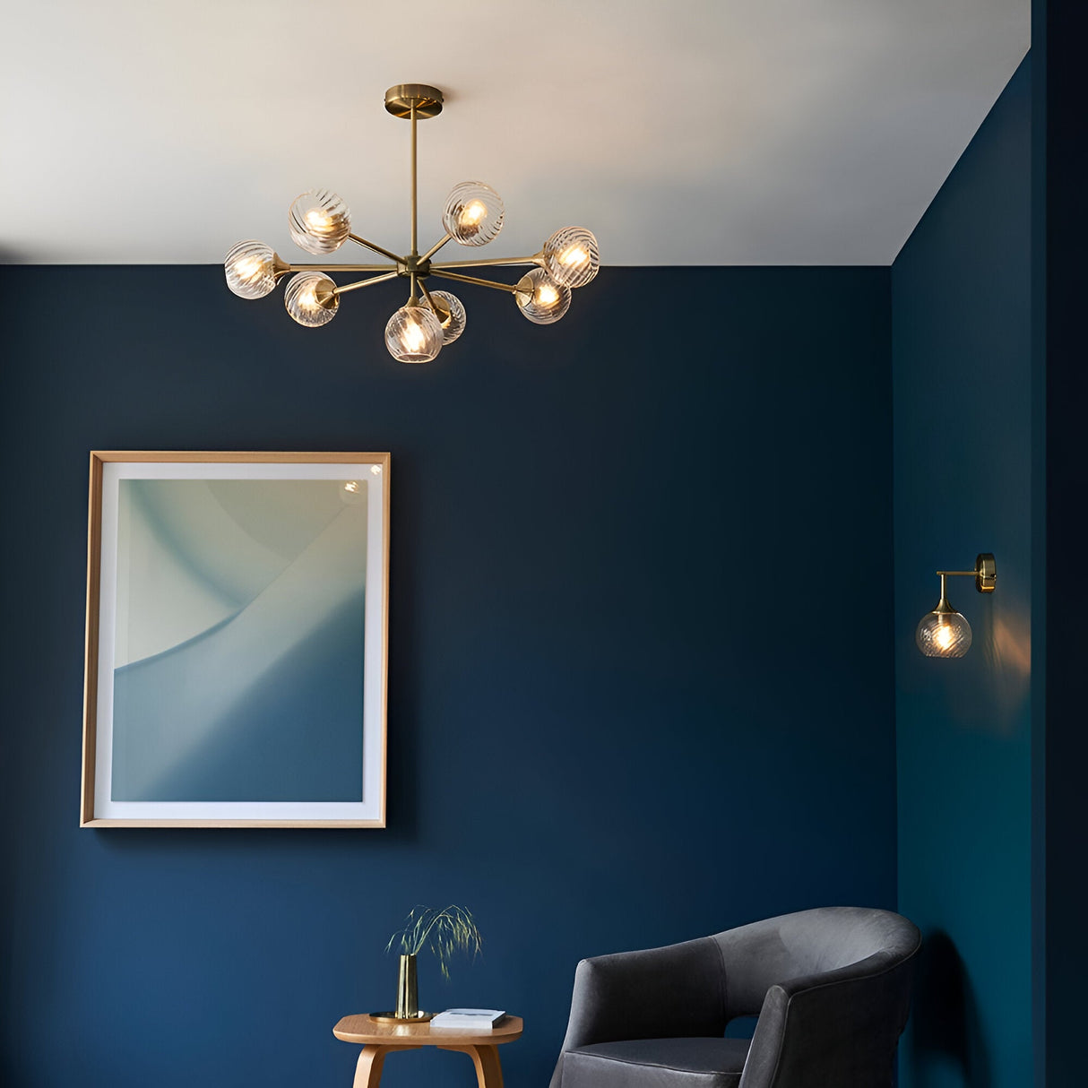 Endon Georgiana 8 light semi-flush pendant in brass with spiral clear glass globes, shown in a dark blue room with framed art and armchair.