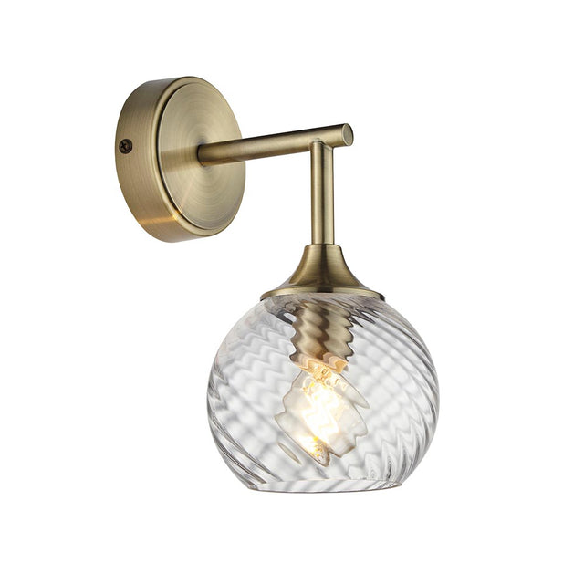 Georgiana Wall Light in Brass, a single-light fitting with round wall plate, angled arm, and twisted spiral-patterned clear glass shade.