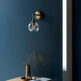 Georgiana Wall Light in brass with a spiral-textured clear glass shade, mounted on a dark blue wall above a side table with a brass vase.
