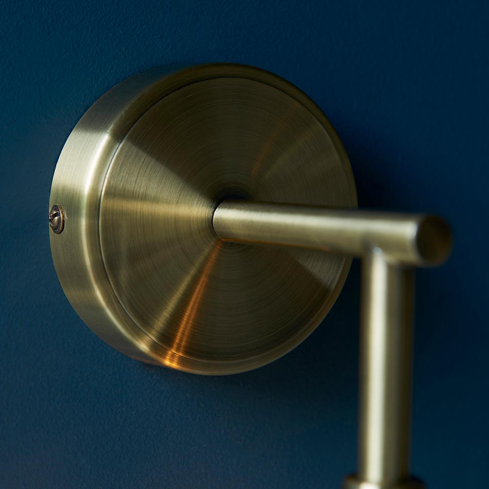 Georgiana Wall Light in brass, close-up of the round backplate and extending arm with fixing screw, shown against a dark blue wall.