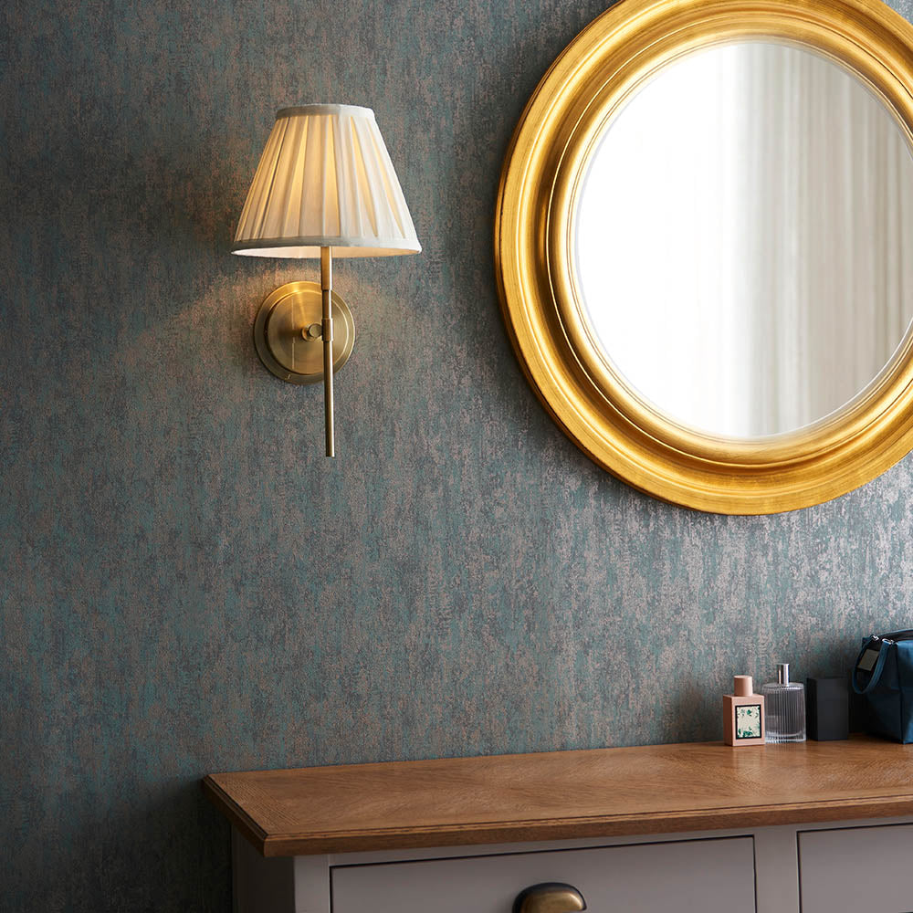 Endon Chartwell wall light with tapered box-pleat cream cotton shade on an antique brass bracket, mounted beside a round gold mirror above a wooden dresser.