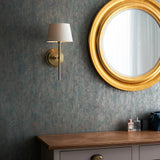 Endon Chartwell wall light in antique brass with a tapered ivory fabric shade, mounted on a textured teal wall beside a round gold-framed mirror.