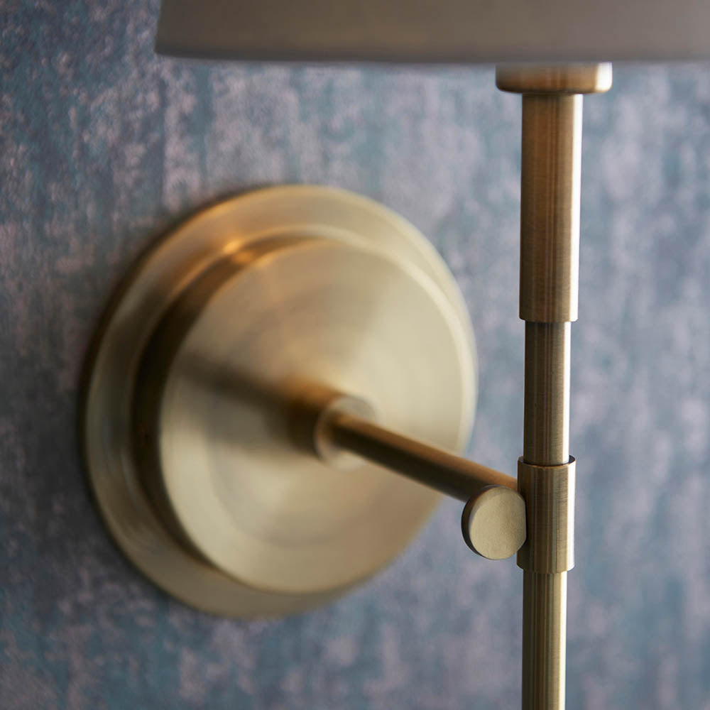 Close-up of the Endon Chartwell wall light's antique brass bracket and round wall plate, showing the slim stem and ivory shade against a mottled blue wall.