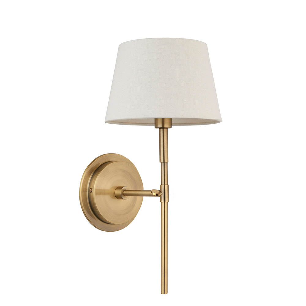 Endon Chartwell wall light with a tapered ivory fabric shade on a slim antique brass bracket and round wall plate, shown against a white background.
