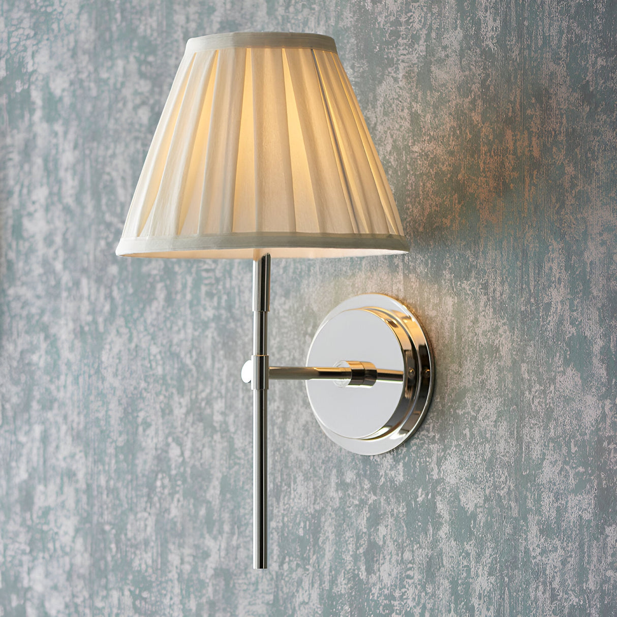 Endon Chartwell wall light with pleated cream cotton tapered shade and polished nickel bracket, mounted on a distressed blue-grey wall.