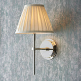 Endon Chartwell wall light with pleated cream cotton tapered shade and polished nickel bracket, mounted on a distressed blue-grey wall.