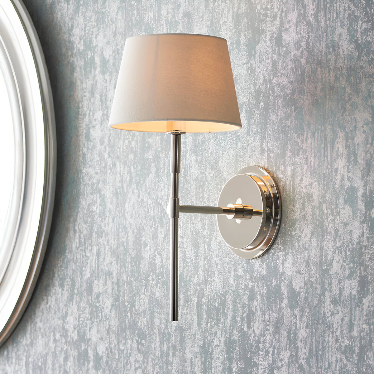 Endon Chartwell wall light in nickel with tapered ivory fabric shade, mounted on a textured grey wall beside a round mirror frame.