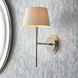 Endon Chartwell wall light in nickel with tapered ivory fabric shade, mounted on a textured grey wall beside a round mirror frame.