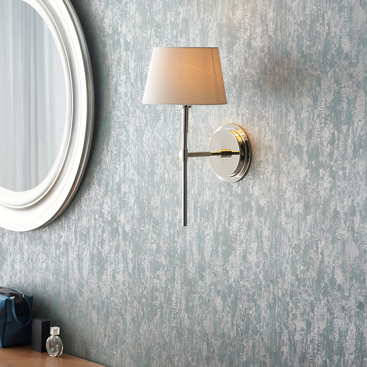 Endon Chartwell wall light with tapered ivory fabric shade and nickel bracket, mounted on a textured blue-grey wall beside a round white-framed mirror.