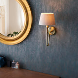 Endon Cliffdon antique brass wall light with tapered ivory fabric shade, mounted on a textured blue wall beside a round gold-framed mirror.