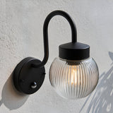 Endon Brackgrove outdoor wall light in black with arched arm, ribbed clear glass globe shade and PIR sensor, mounted on a textured white exterior wall.