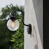Endon Brackgrove outdoor wall light in black with arched arm, ribbed clear glass globe shade and PIR sensor, mounted on a rendered exterior wall.