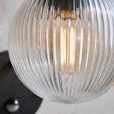 Close-up of the Endon Brackgrove outdoor wall light showing its clear ribbed glass globe shade illuminated by a filament bulb against a black fitting.