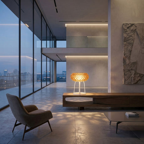 A modern, minimalist living space with floor-to-ceiling windows, a sculpted armchair, a low coffee table, and the Briller LED Table Lamp - Gold glowing on a sleek wooden console, overlooking a city skyline at dusk.