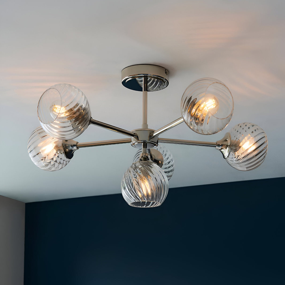 Georgiana 6-light semi-flush ceiling light in nickel, with ribbed glass globe shades on splayed arms from a central plate, mounted on a white ceiling.
