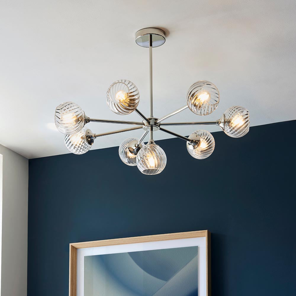 Endon Georgiana 8 light semi-flush pendant with spiral-cut clear glass globe shades on a nickel sputnik frame, mounted on a ceiling above a dark blue wall.