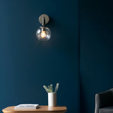 Endon Georgiana wall light in nickel with a spiral-patterned clear glass globe shade, mounted on a dark blue wall above a wooden side table.