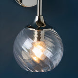 Endon Georgiana wall light in nickel with a spiral-patterned clear glass globe shade and illuminated E14 bulb, shown against a dark blue wall.