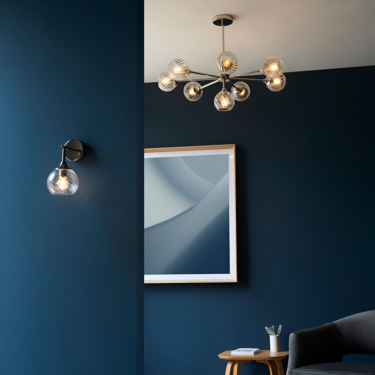 Endon Georgiana wall light in nickel with spiral-patterned clear glass shade, mounted on a deep blue wall beside a framed print and matching chandelier.