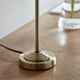 Close-up of the Endon Brenley table lamp's tiered antique brass base and slim stem on a wooden surface, with black flex trailing to the side.