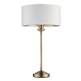 Endon Brenley table lamp with slim antique brass stem, stepped base and white drum shade with gold metallic inner, shown on a plain background.
