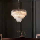 Endon Cranshaw 12 light tiered pendant in polished chrome with ribbed clear glass tubes, hanging from a chain above a dining table against a dark panelled wall.