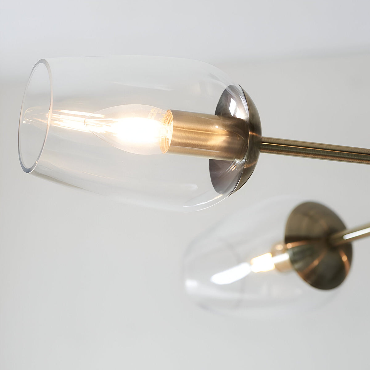 Close-up of the Caldworth 6 Light Pendant in brass, showing clear blown glass shades, exposed bulbs, and slender brass arms against a plain background.