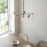 Endon Caldworth 6 Light Pendant in nickel with slender curved arms and clear blown glass shades, shown above a dining table beside a tall window.