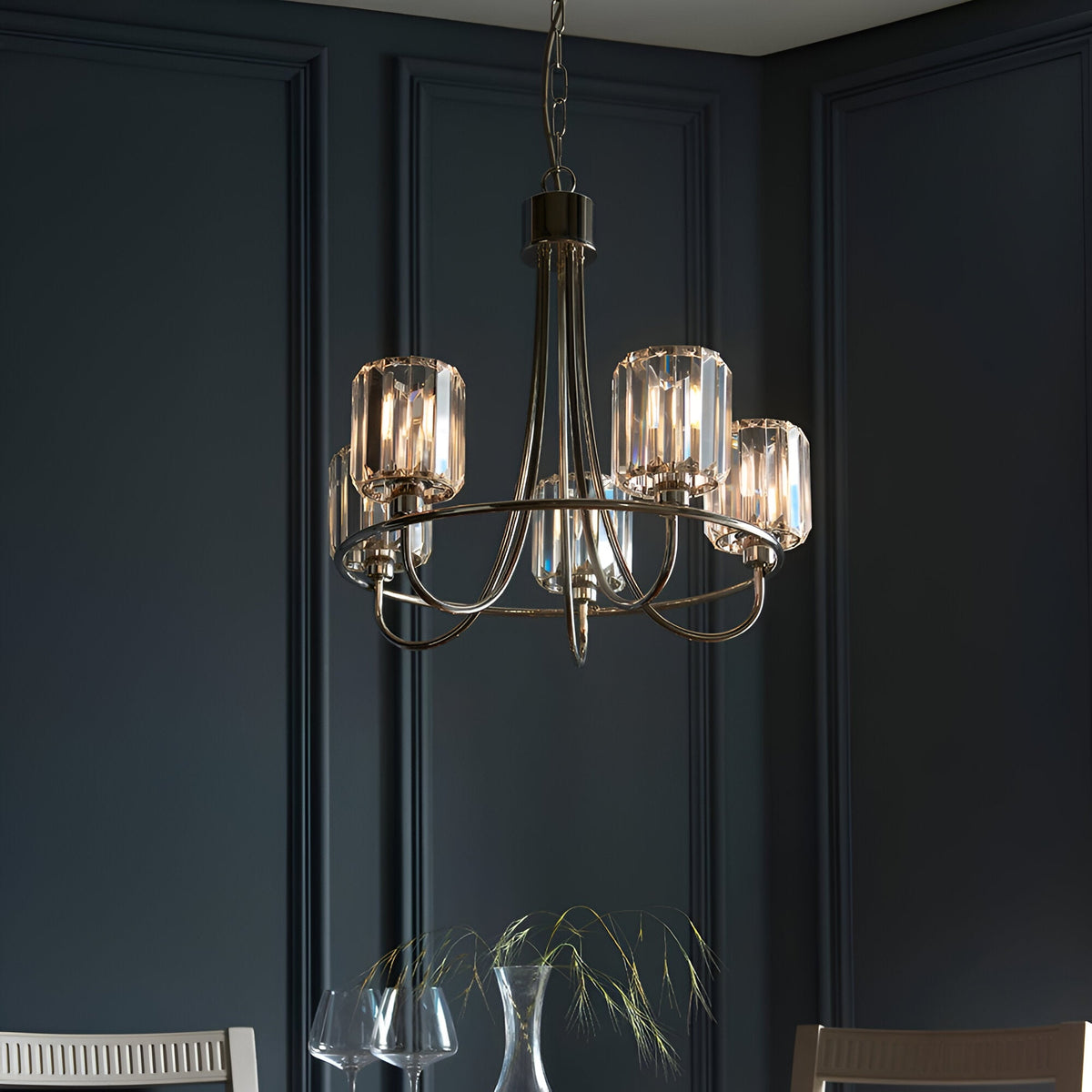 Clementine 5 Light Pendant in nickel, with curved arms and cut faceted glass shades, hanging above a dining table in a dark panelled room.