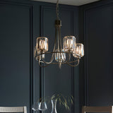 Clementine 5 Light Pendant in nickel, with curved arms and cut faceted glass shades, hanging above a dining table in a dark panelled room.