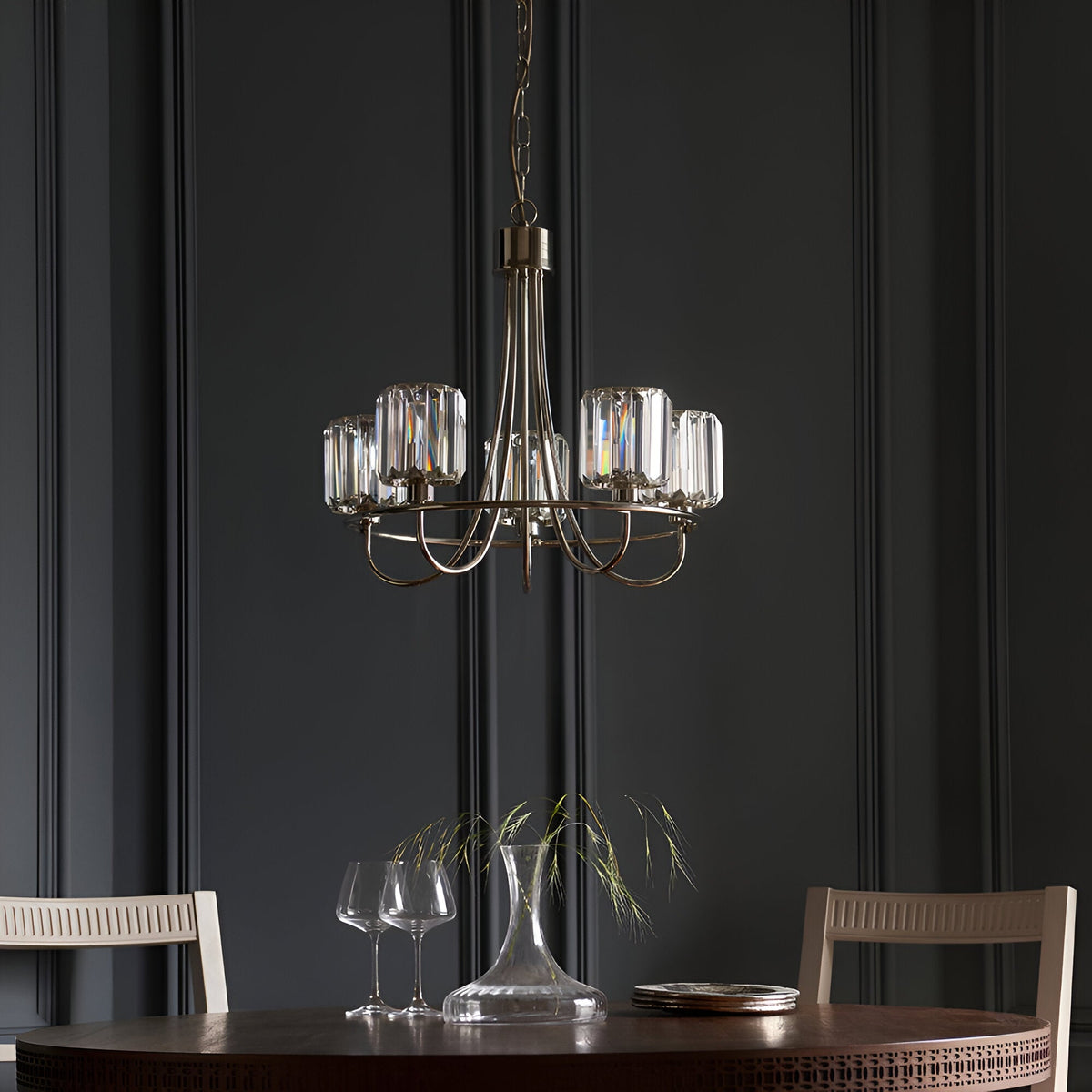 Clementine 5 Light Pendant in nickel with curved arms and faceted glass shades, hung above a dining table in a dark panelled room.