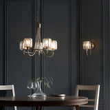Clementine 5 Light Pendant in nickel with faceted glass shades on curved arms, hung above a dining table in a dark panelled room.