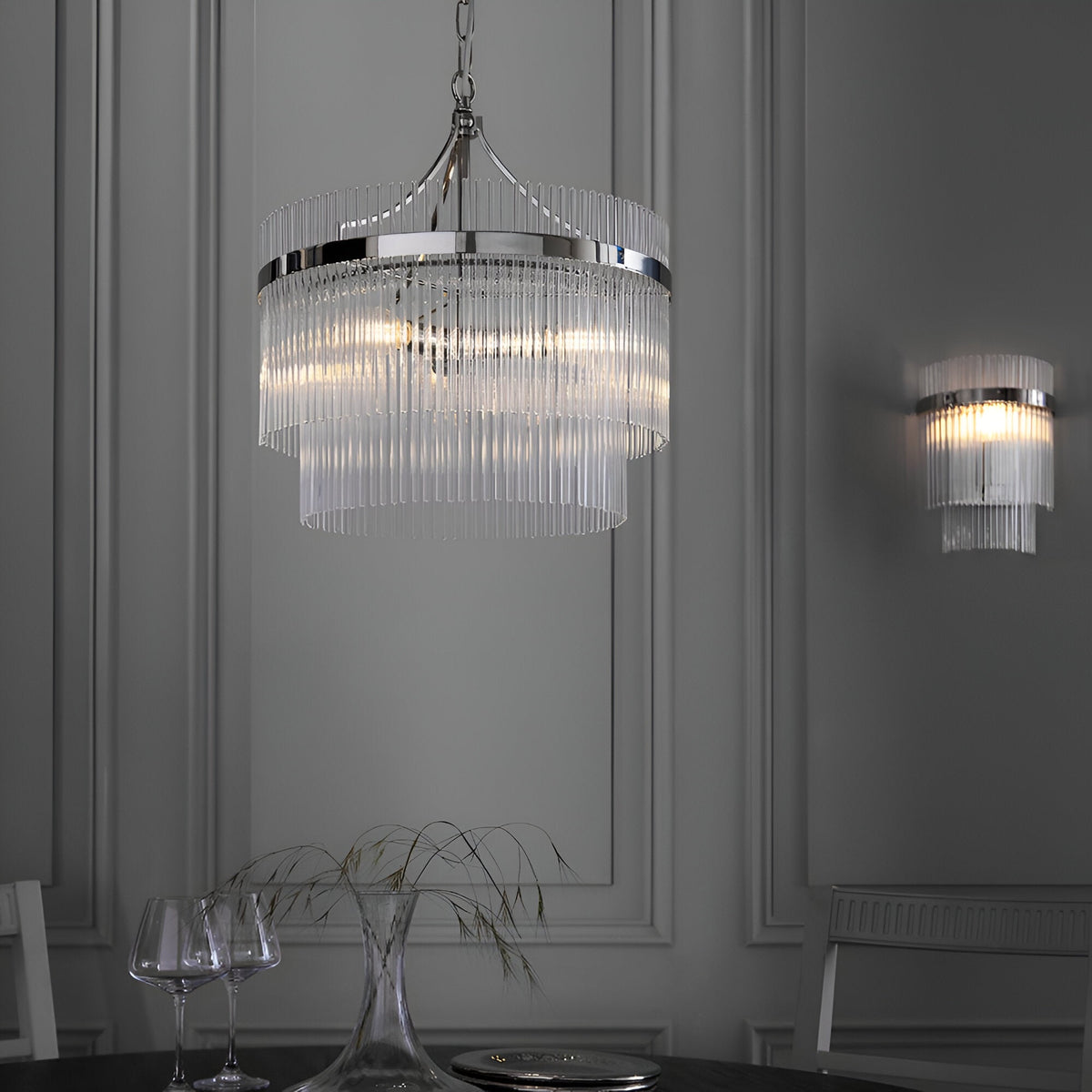 Beaumont 3 Light Pendant in nickel with tiered clear glass rods, hung on a chain above a dining table in a grey-panelled room, with a matching wall light.