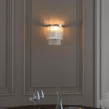 Endon Beaumont wall light in nickel with tiered clear glass rods, illuminated on a panelled grey wall above a dining table with glassware.