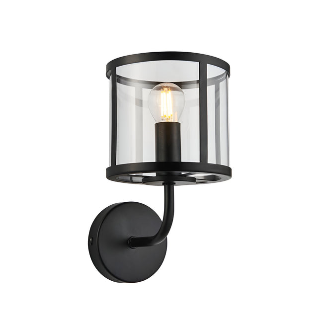 Endon Ellery wall light in matt black with a clear cylindrical glass shade, curved arm, round backplate and single E14 filament bulb.