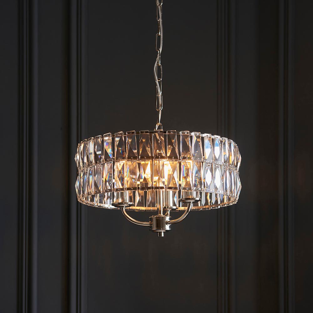 Bevmont 3 Light Pendant in nickel with a drum shade of faceted crystal glass on a chain suspension, hanging against a dark panelled wall.