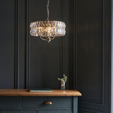 Bevmont 3 Light Pendant in nickel with cut faceted glass panels and chain suspension, shown lit above a dark wood sideboard in a moody dark-panelled room.