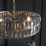 Endon Bevmont 5 light pendant in nickel with a wide drum frame of clear cut faceted glass panels, suspended on a chain against a dark panelled wall.