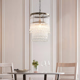 Bramgrove Pendant in antique brass with tiered clear glass droplets, hung above a dining table in a soft pink-toned room.