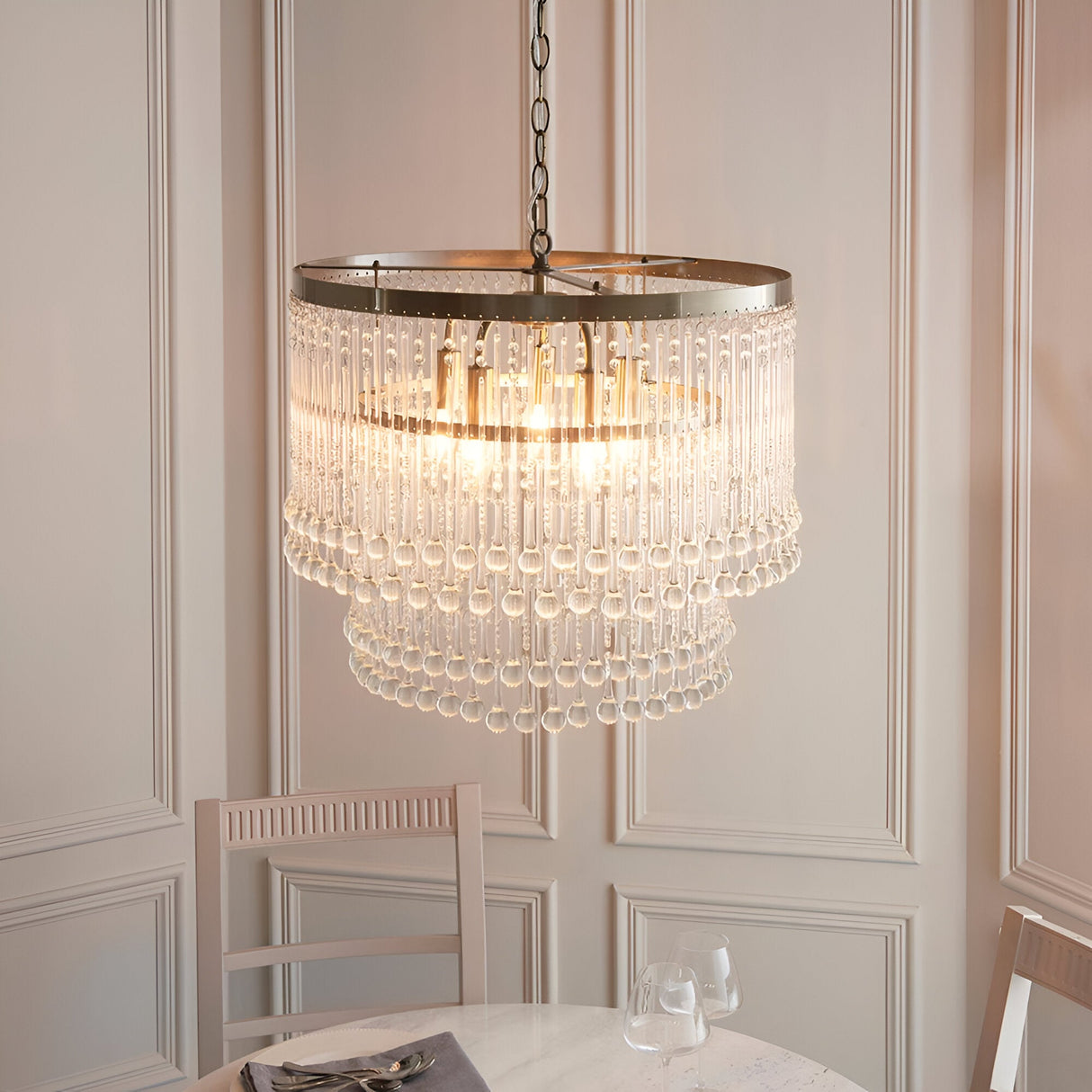 Endon Bramgrove 5 light tiered pendant with clear glass droplets and antique brass frame, suspended by chain above a dining table in a panelled room.