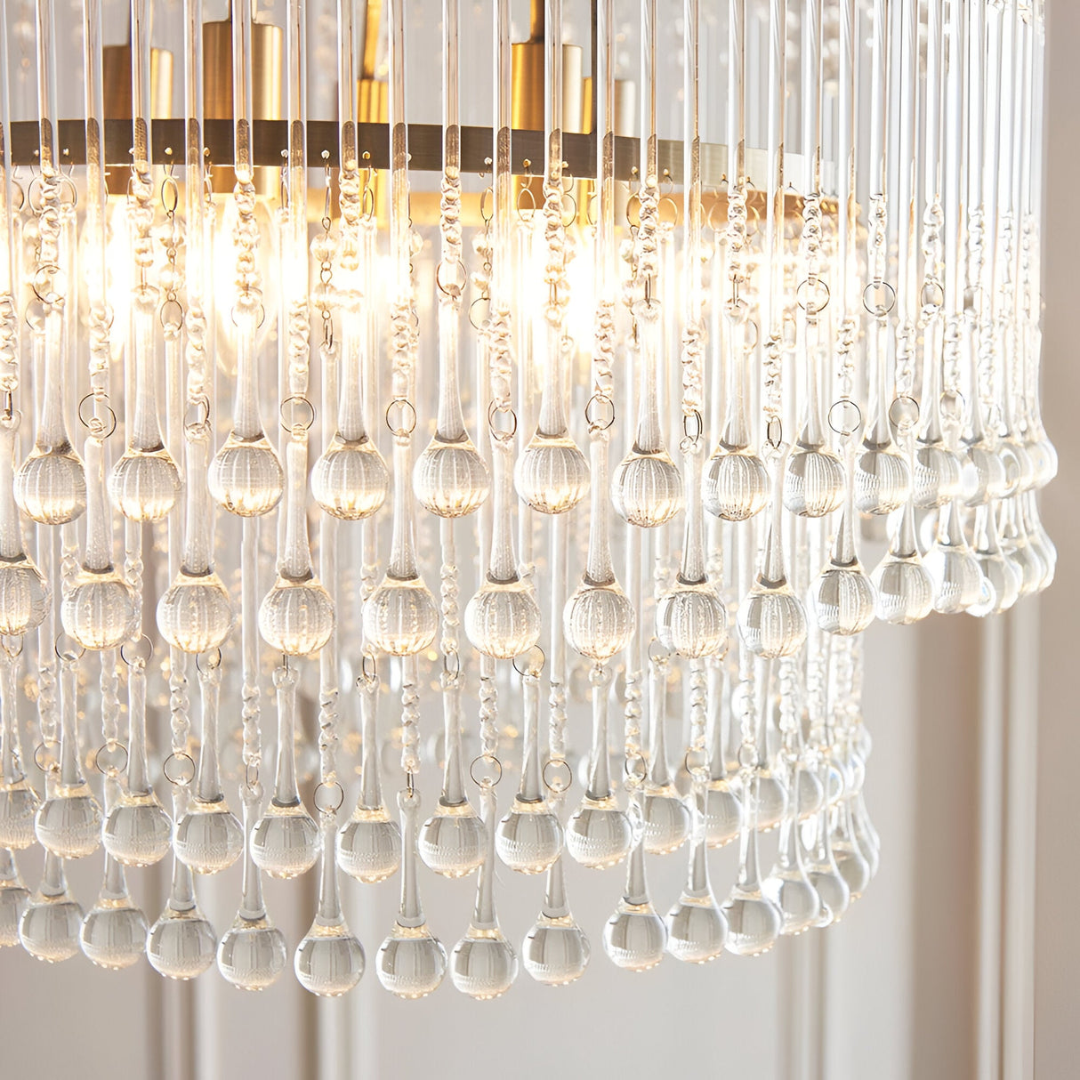 Close-up of Endon Bramgrove 5 Light Pendant in antique brass, showing tiered clear glass droplets and lit E14 lamps within the frame.