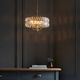 Endon Bevmont 3 light pendant in brass with faceted crystal drum shade, suspended from a chain above a dark panelled wall and wooden sideboard.