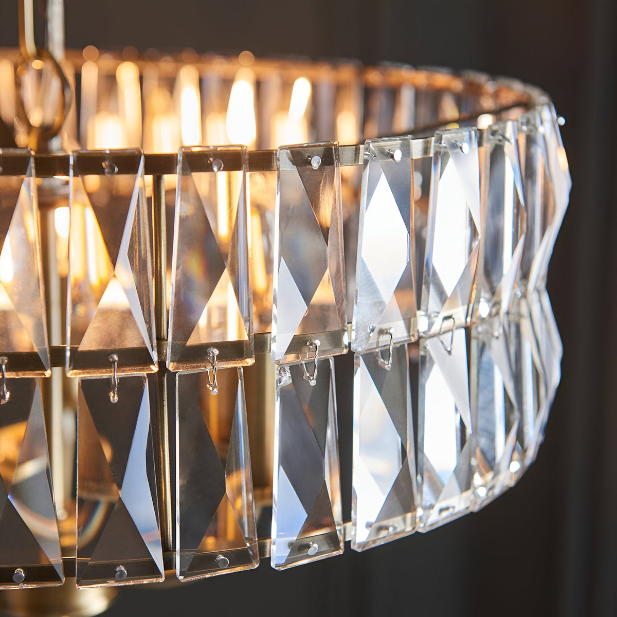 Close-up of the Endon Bevmont 3 light pendant showing tiered clear cut faceted glass panels on a brass frame with illuminated E14 lamps.