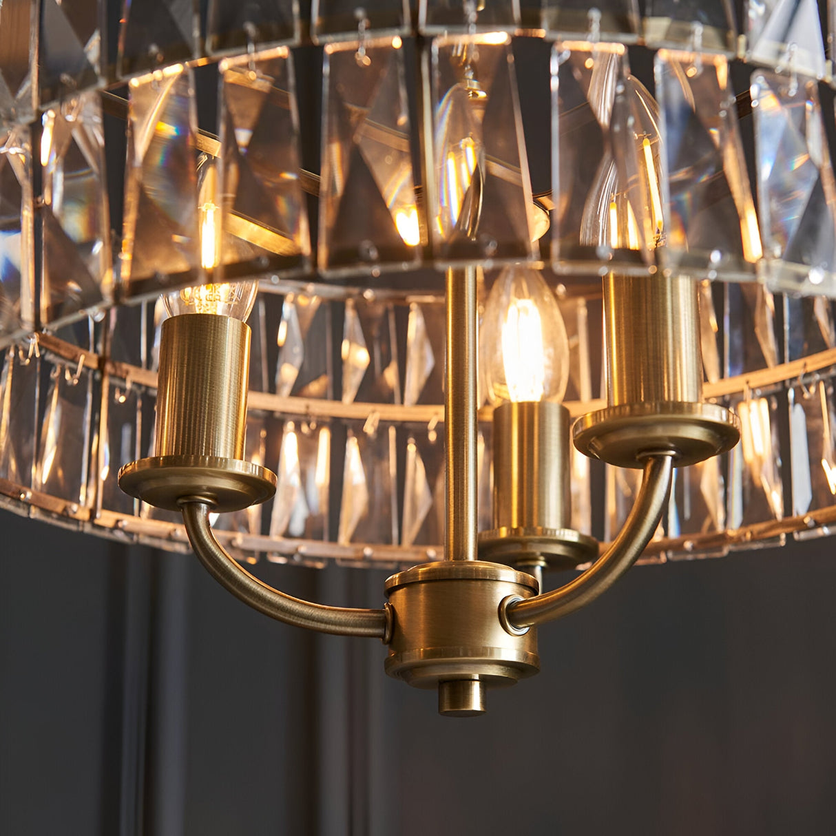 Close-up of the Endon Bevmont 3 light pendant in brass, showing curved arms, E14 candle lamps and a tiered drum shade of cut faceted glass.