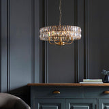 Bevmont 5 Light Pendant in brass with faceted crystal glass panels and five candle-style arms, hung above a dark green sideboard in a moody living room setting.
