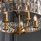 Bevmont 5 Light Pendant in antique brass, close-up of candle-style arms and E14 bulbs beneath a faceted crystal glass drum shade.