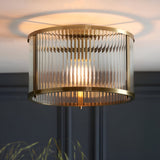 Rothbury flush ceiling light in antique brass, round drum shade with vertical glass rods and visible bulb, mounted on a dark ceiling.