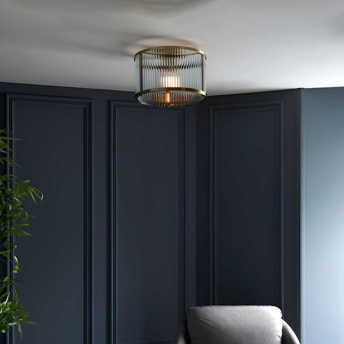 Rothbury flush ceiling light in antique brass with ribbed glass shade, mounted on a white ceiling above dark panelled walls in a living room.