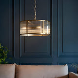 Rothbury 3 Light Pendant in antique brass with ribbed glass panel shades, hanging on a chain above a sofa against dark panelled walls.